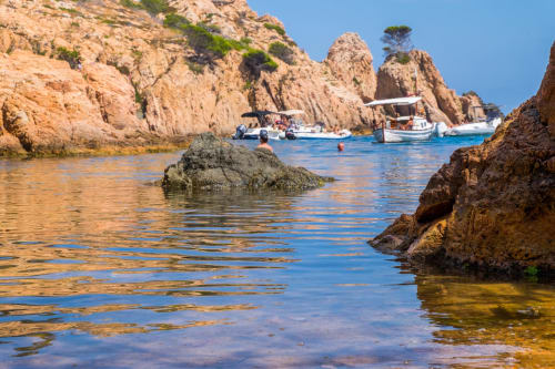 Cala pintoresca de Llafranc con aguas turquesas, acantilados rocosos y barcas amarradas cerca del Hotel La Muntanya