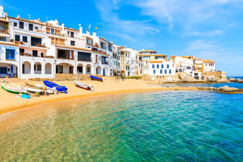 Edificios frente al mar del Hotel La Muntanya en Llafranc, España con barcas coloridas, playa arenosa y aguas turquesas del Mediterráneo