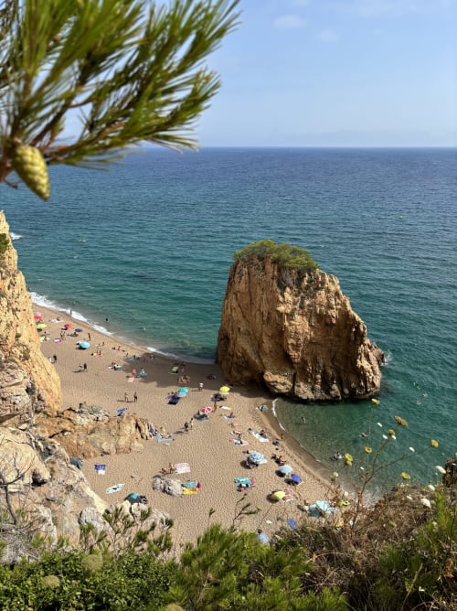 Pintoresca cala de playa en Llafranc con acantilado dorado, rocas salientes, aguas turquesas del Mediterráneo y bañistas