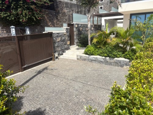 Elegante entrada com portão das Residências BHF, villa de luxo em Arco da Calheta, com muros de pedra, jardins tropicais e design moderno