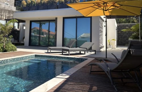 Área de piscina da villa familiar de luxo em BHF Residences com espreguiçadeiras, guarda-sol amarelo e moderno edifício branco com vista panorâmica
