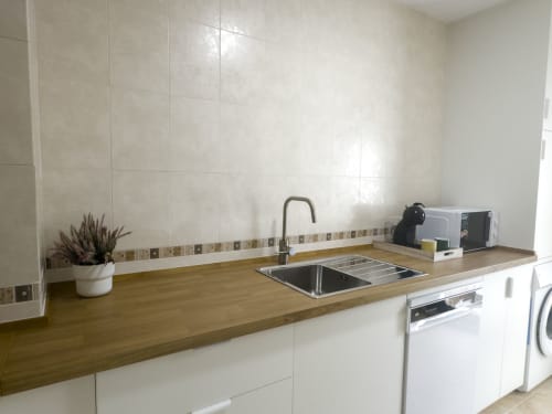 Cocina moderna con encimera de madera, fregadero de acero inoxidable, muebles blancos y azulejos decorativos en la cabaña