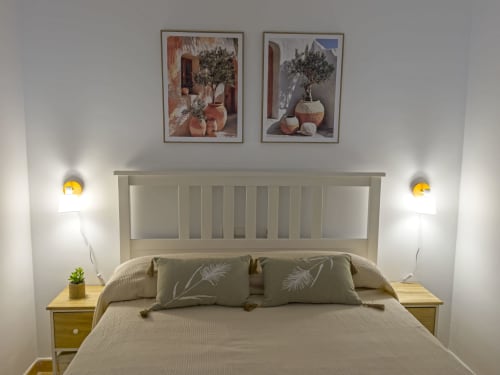 Dormitorio acogedor en la casita Living Sur en Sanlúcar de Barrameda con cabecero beige, cojines decorativos, mesillas de madera y