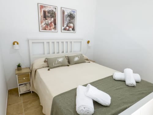 Dormitorio moderno en la casa rural Living Sur de Sanlúcar de Barrameda con cama blanca, cuadros enmarcados, mesita de noche y elementos blancos enrollados