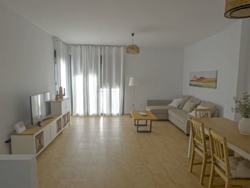 Luminosa sala de estar de planta abierta en la casa Alzara de Living Sur, Sanlúcar de Barrameda, con sofá beige, mesa de comedor, televisor y