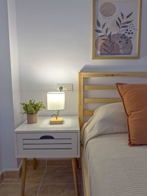 Habitación moderna en Living Sur Sanlúcar con cama de madera, lámpara de mesita, planta en maceta y arte botánico en la pared
