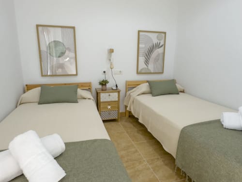 Habitación doble con camas crema, almohadas verdes, mesillas de madera y arte botánico en Living Sur, Sanlúcar de Barrameda