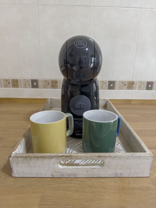 Cafetera Dolce Gusto negra con tazas amarilla y verde en bandeja de madera en Living Sur, Sanlúcar de Barrameda