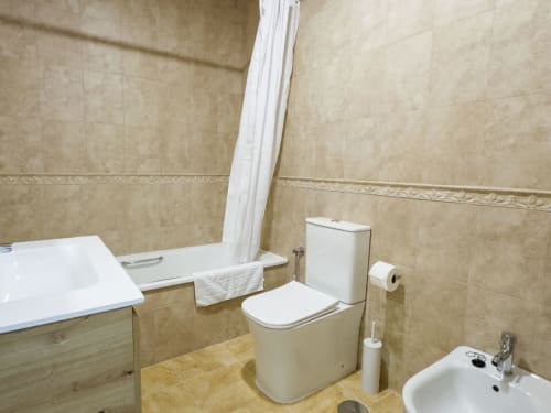 Baño moderno en apartamento Alzara de Living Sur, Sanlúcar de Barrameda con inodoro, lavabo, bañera y paredes de azulejos beige