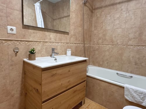 Baño moderno con tocador de madera, lavabo blanco, espejo y bañera en la casita Living Sur de Sanlúcar de Barrameda