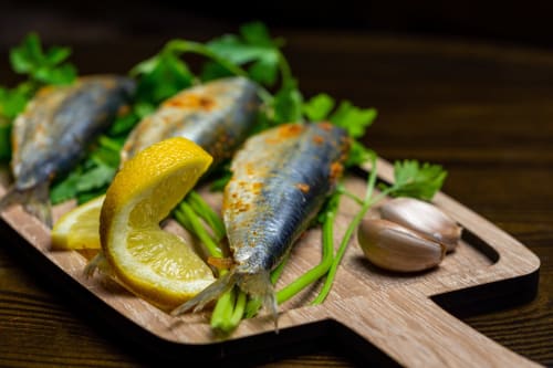 Sardinas a la parrilla con limón y perejil sobre tabla de madera en Hotel La Muntanya, Llafranc