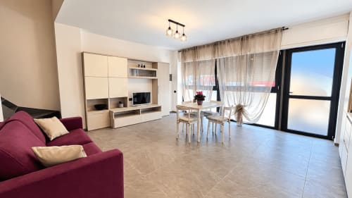 Ampio soggiorno dell'appartamento Tolstoi 13.15 a Saronno con divano bordeaux, zona pranzo e balcone con vista sulla città