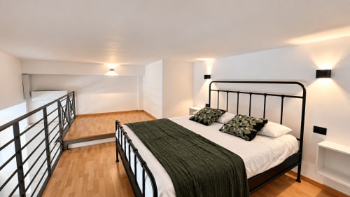 Camera da letto moderna dell'appartamento Tolstoi 13 a Saronno con letto in metallo, biancheria bianca, pavimenti in legno e vista sulla città