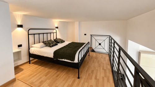 Camera da letto moderna dell'appartamento Tolstoi 13 a Saronno con letto in metallo nero, pavimenti in legno e zona mezzanino