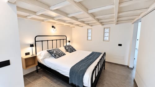 Camera moderna dell'appartamento Tolstoi 13 a Saronno con letto in metallo nero, biancheria bianca e comodini in legno