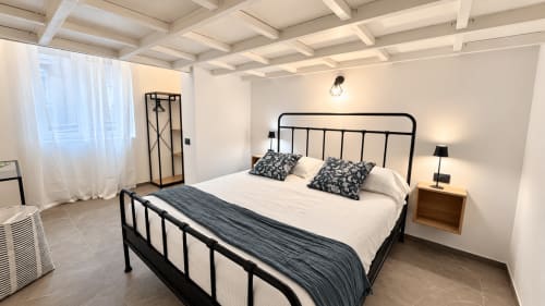 Camera moderna a Tolstoi 13.15 di Saronno con letto in metallo nero, biancheria bianca, comodino in legno e vista sulla città