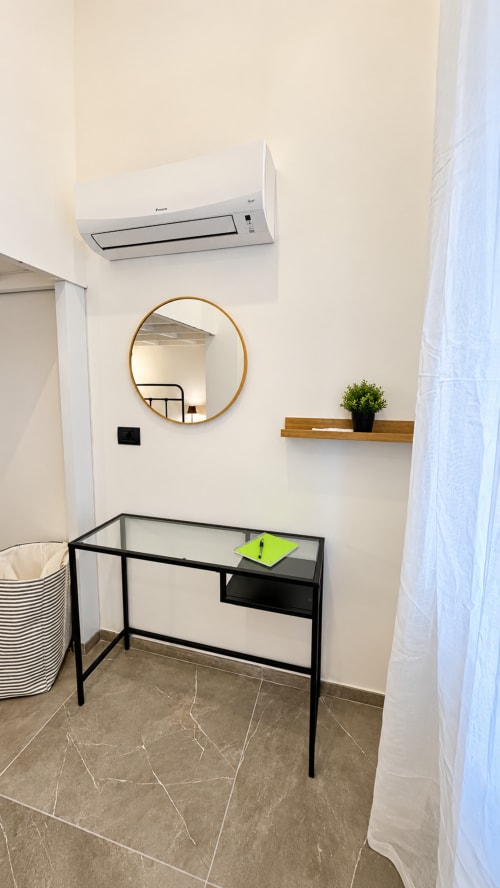 Spazio di lavoro moderno in appartamento Tolstoi 13, Saronno: scrivania in vetro, specchio rotondo, ripiano in legno, climatizzatore e pavimenti in marmo