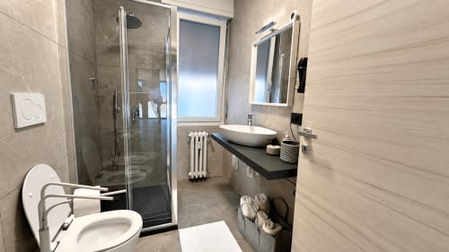 Bagno moderno dell'appartamento Tolstoi 13 a Saronno con doccia, lavabo in ceramica bianca, toilette e specchio
