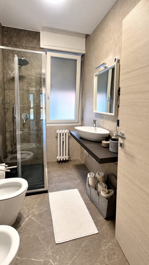 Moderno bagno dell'appartamento Tolstoi 13 a Saronno con lavabo a bacinella, cabina doccia e piastrelle in legno chiaro
