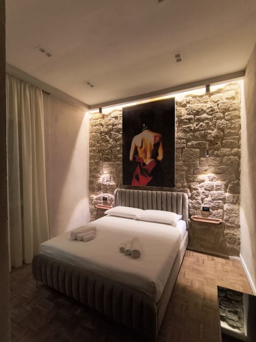 Camera da letto moderna a Napoli con muri in pietra a vista, biancheria bianca, illuminazione d'accento e opere d'arte contemporanea presso Plebiscito Suite
