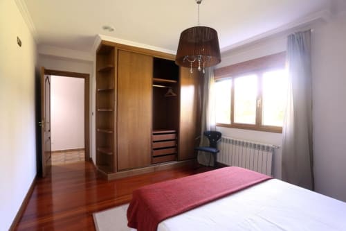 Modern bedroom at A Quinta de Lapido cottage with wooden wardrobe, white bed, red runner, and bright windows