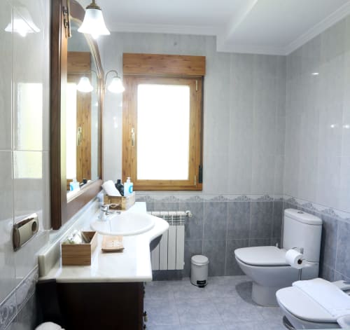 Modern bathroom at A Quinta de Lapido cottage with white sink, toilet, and gray tile walls with wooden window frame