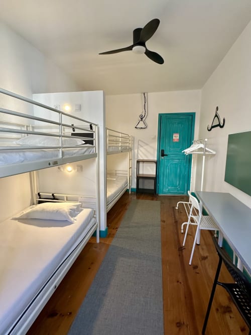 Quarto compartilhado com quatro beliches em My Hostel Guimarães, estrutura em metal branco, piso de madeira e porta azul-turquesa