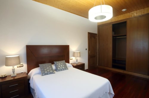 Modern bedroom at A Quinta de Lapido cottage with dark wood bed, white linens, pendant lighting, and wooden ceiling