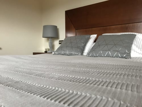 Cozy bedroom at A Quinta de Lapido cottage with textured white bedding, gray patterned pillows, dark wooden headboard, and