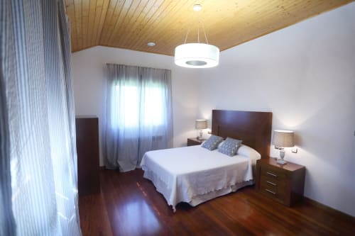 Spacious cottage bedroom at A Quinta de Lapido with wooden ceiling, queen bed, dark nightstands, and natural light from