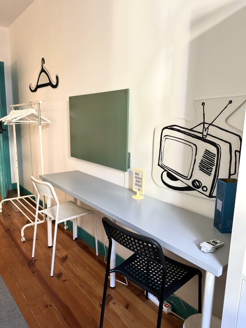 Espaço de trabalho de albergue em Guimarães com escrivaninha, cadeiras, quadro verde e arte mural com TV em piso de madeira