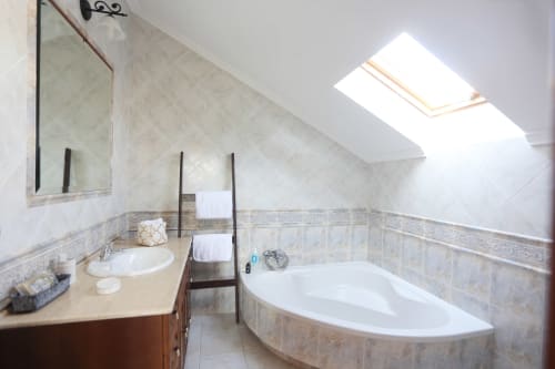 Bright attic bathroom at A Quinta de Lapido cottage with skylight, corner tub, sink, and beige tile walls.
