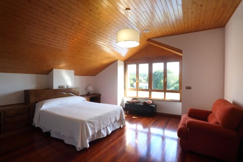 Spacious cottage bedroom at A Quinta de Lapido with wooden ceiling, white bed, red armchair, and large windows overlooking