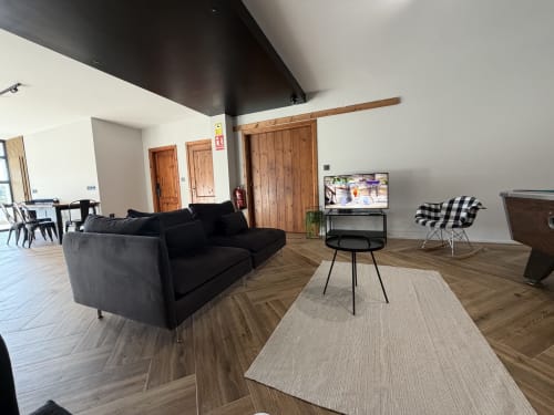 Modern living room at A Quinta de Lapido cottage with black sofa, wooden beams, and TV in Spanish countryside