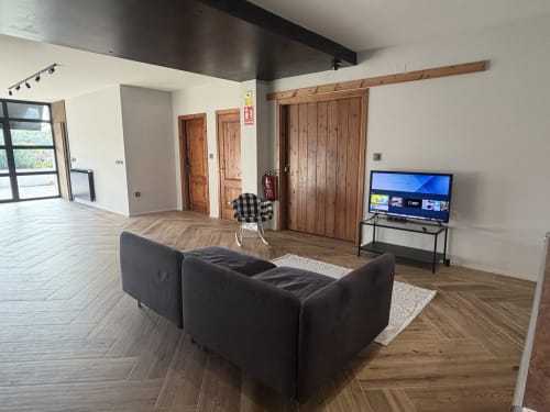 Spacious cottage living area at A Quinta de Lapido with black sofa, wooden doors, TV, and modern wood flooring