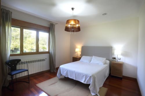 Amplio dormitorio en A Quinta de Lapido con cama de matrimonio, lámpara colgante, suelos de madera, gran ventana y mobiliario moderno