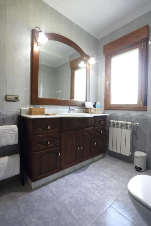 Baño moderno en A Quinta de Lapido con tocador de madera oscura, espejo grande, radiador calefactor y suelo de baldosas