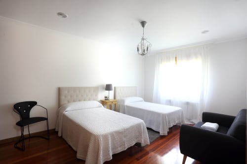 Luminosa habitación doble en A Quinta de Lapido con ropa de cama blanca, suelo de madera, lámpara colgante y zona de estar en España