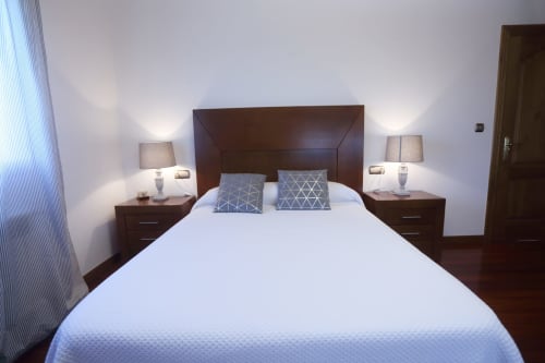 Dormitorio moderno en A Quinta de Lapido con ropa de cama blanca, muebles de madera oscura, almohadas geométricas y lámparas de noche en España