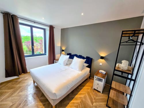 Modern bedroom at Vindihouses in Épinac with queen bed, blue headboard, wooden floors, grey accent wall, and garden views