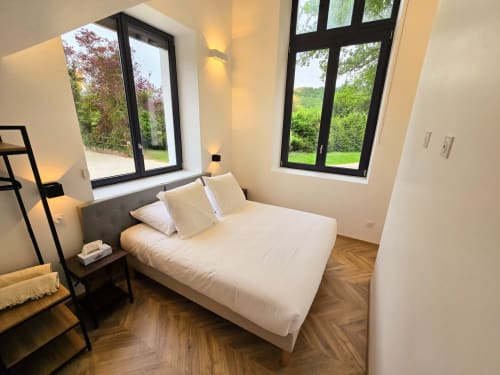 Modern bedroom with queen bed, white linens, black-framed windows overlooking green gardens at Vindihouses, Épinac