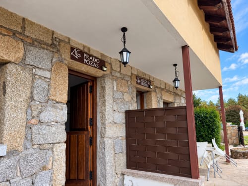 Entrada de Prado Pozas en ALTOGREDOS, edificio de piedra con puerta de madera y linternas en Hoyos del Espino