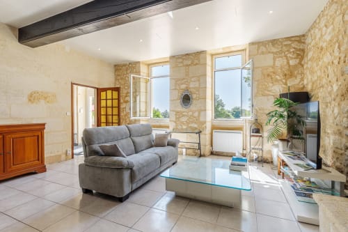 Modern living room at Domaine De Pimpine with stone walls, gray sofa, and river views through large windows
