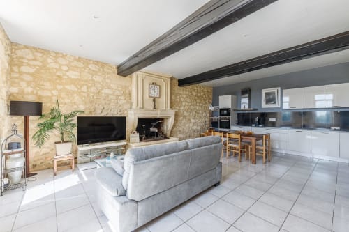 Spacious open-plan living area at Domaine De Pimpine with stone walls, fireplace, gray sofa, TV, and modern white kitchen