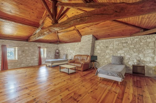Spacious loft bedroom at Domaine De Pimpine with wooden beams, stone walls, beds, leather armchair, and river views in Galgon