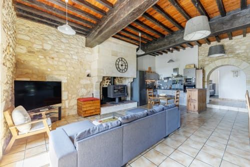 Spacious open-plan living area at Domaine De Pimpine with exposed beams, stone walls, TV, blue sofa, and kitchen in Galgon