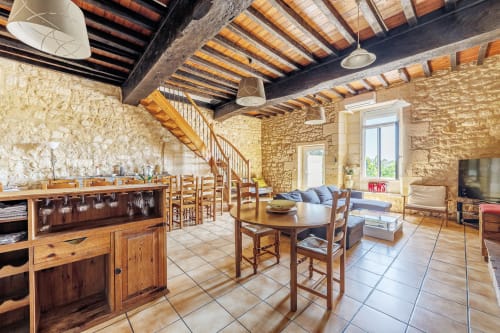 Rustic stone dining room with wooden beams, staircase, and kitchen area at Domaine De Pimpine, Galgon