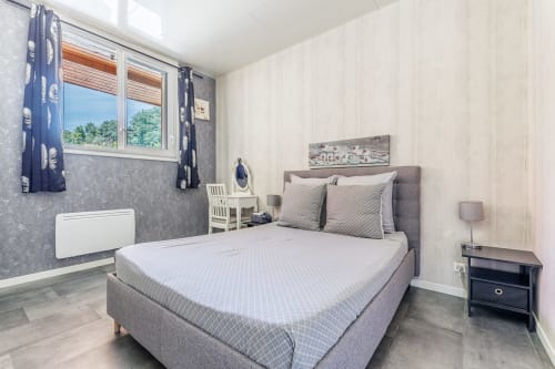 Modern bedroom at Domaine De Pimpine with gray upholstered bed, beige walls, and river views through windows at La Maison en