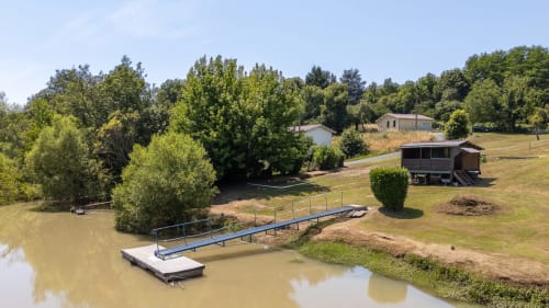 Riverside dock and property grounds at Domaine De Pimpine in Galgon with lush trees and rustic buildings