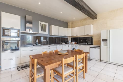 Modern kitchen and dining area at Domaine De Pimpine cottage with wooden table, white cabinetry, and black backsplash in